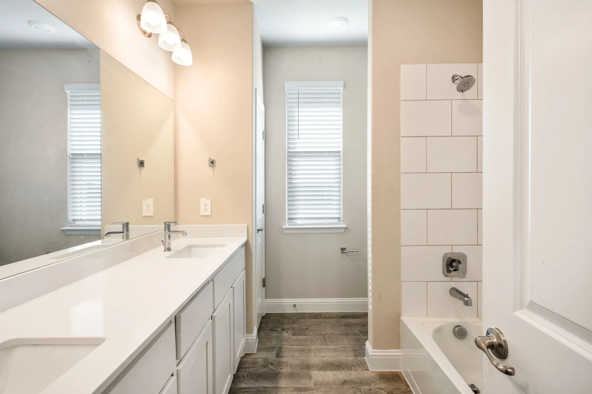Dual vanity with integrated sinks and white countertops, wood-finish flooring, full-width mirror, and a tiled shower/tub combination