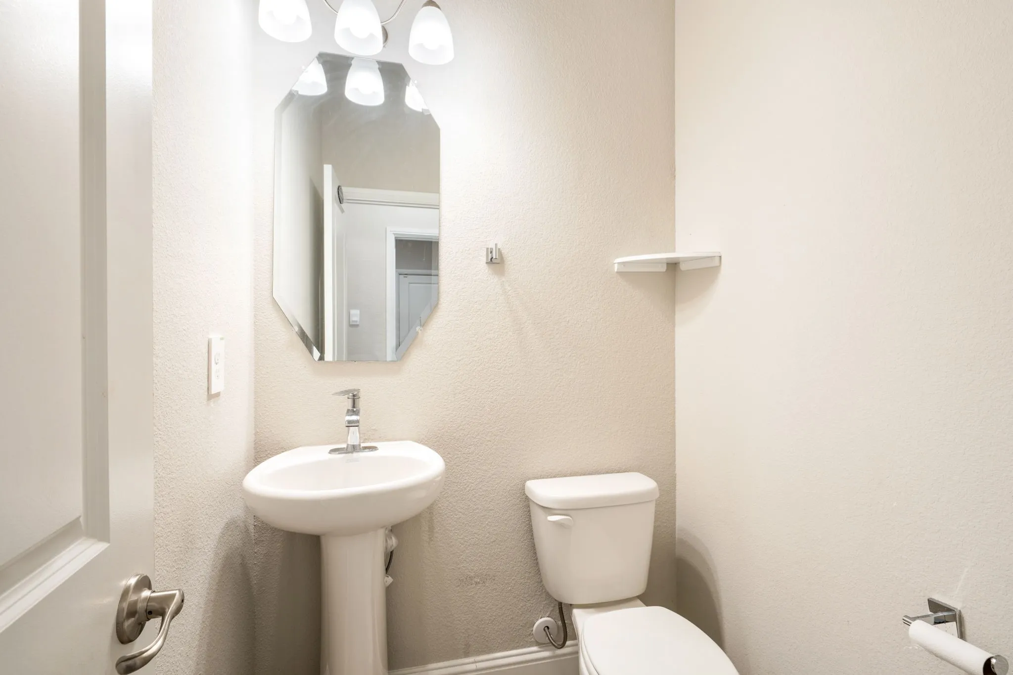 Pedestal sink with chrome faucet, octagonal wall mirror, and overhead vanity lighting