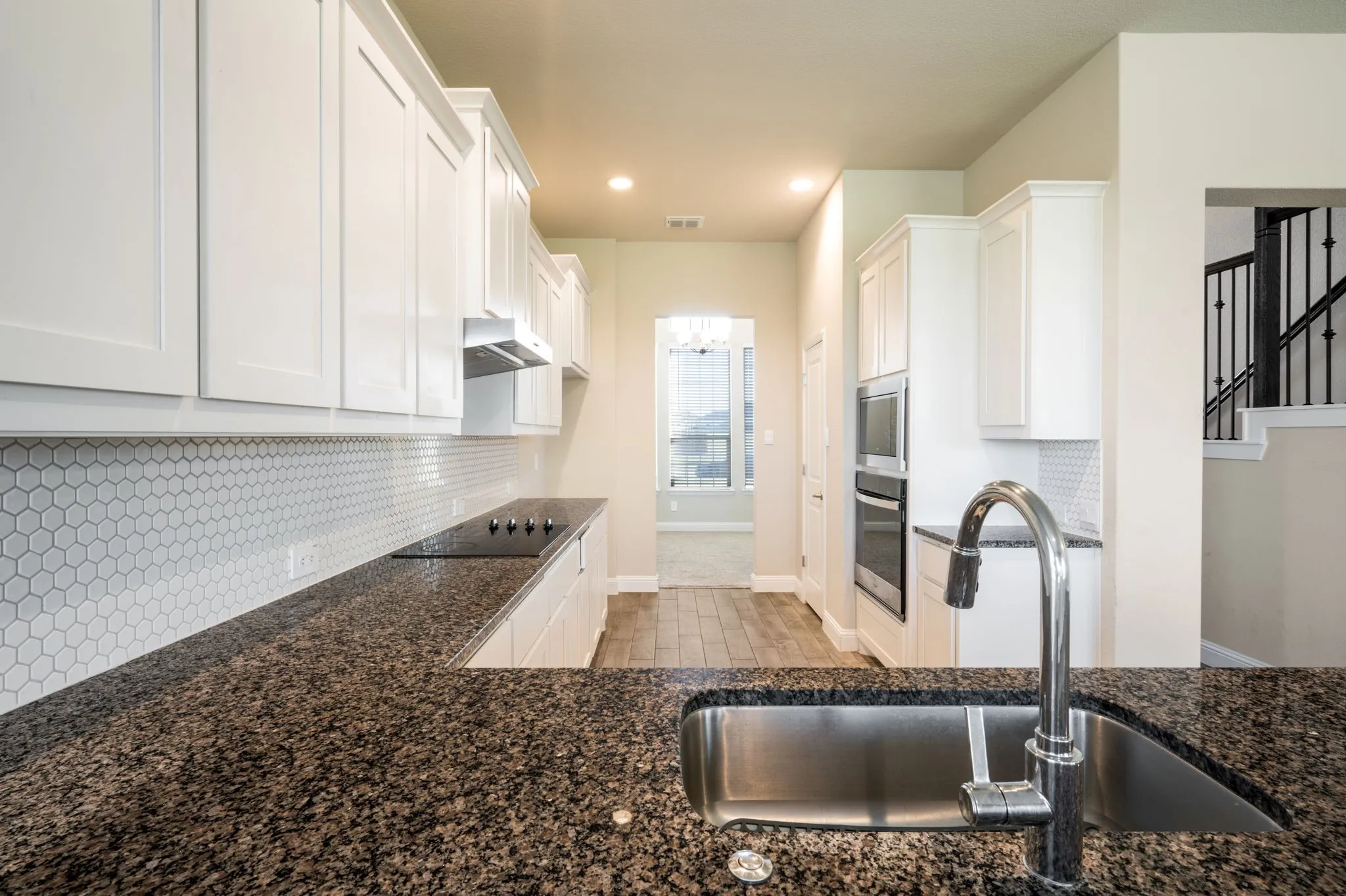 Kitchen featuring white shaker cabinetry, dark speckled countertops, a hexagon tile backsplash, stainless steel double ovens, and a stainless steel undermount sink with a gooseneck faucet