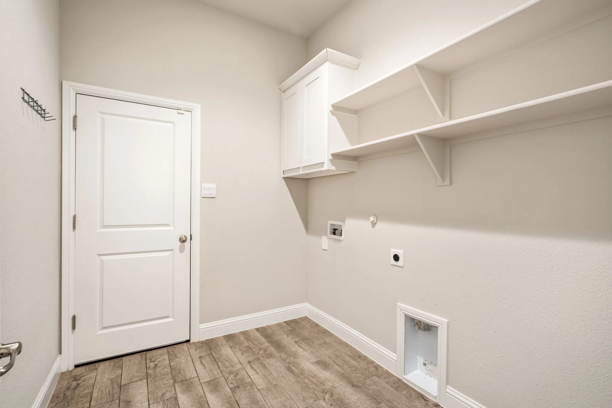 Laundry room featuring wood-finish flooring, built-in wall shelving, a wall-mounted cabinet, and appliance hookups