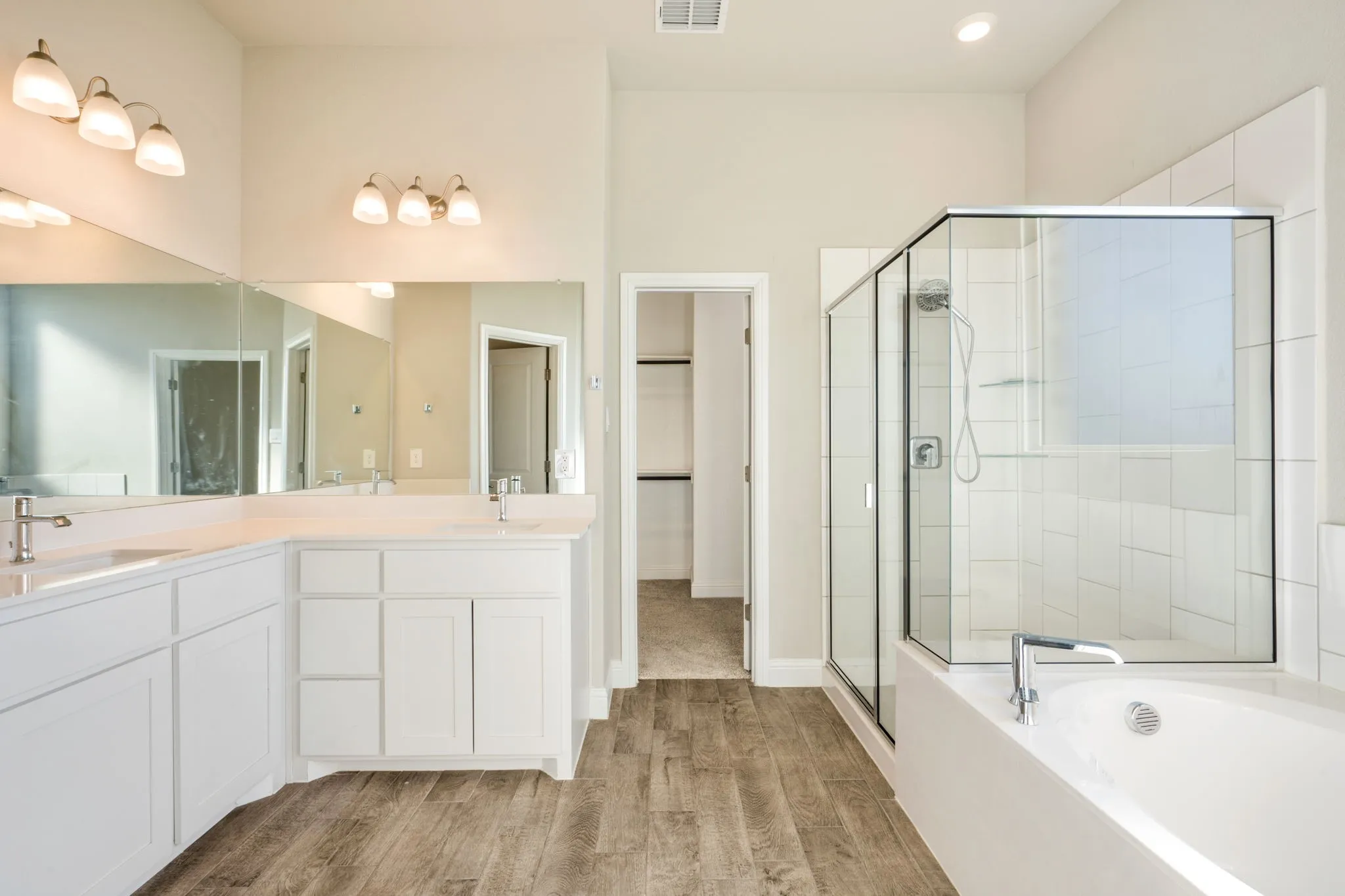 Dual vanity with white cabinetry, wood-finish flooring, glass-enclosed shower, and built-in tub
