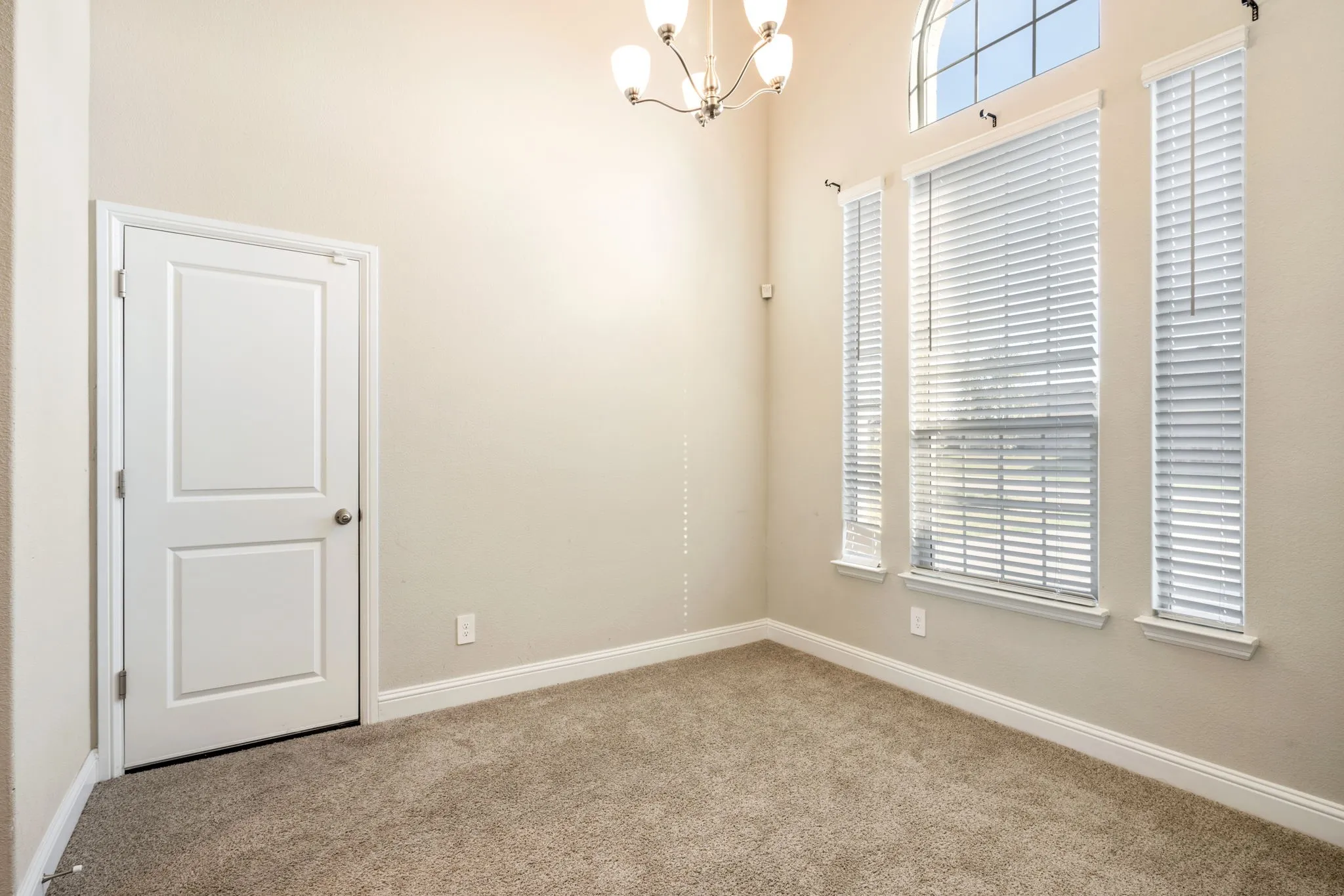 Vaulted ceiling with an arched transom window, a multi-light chandelier, three vertical windows, and carpet flooring