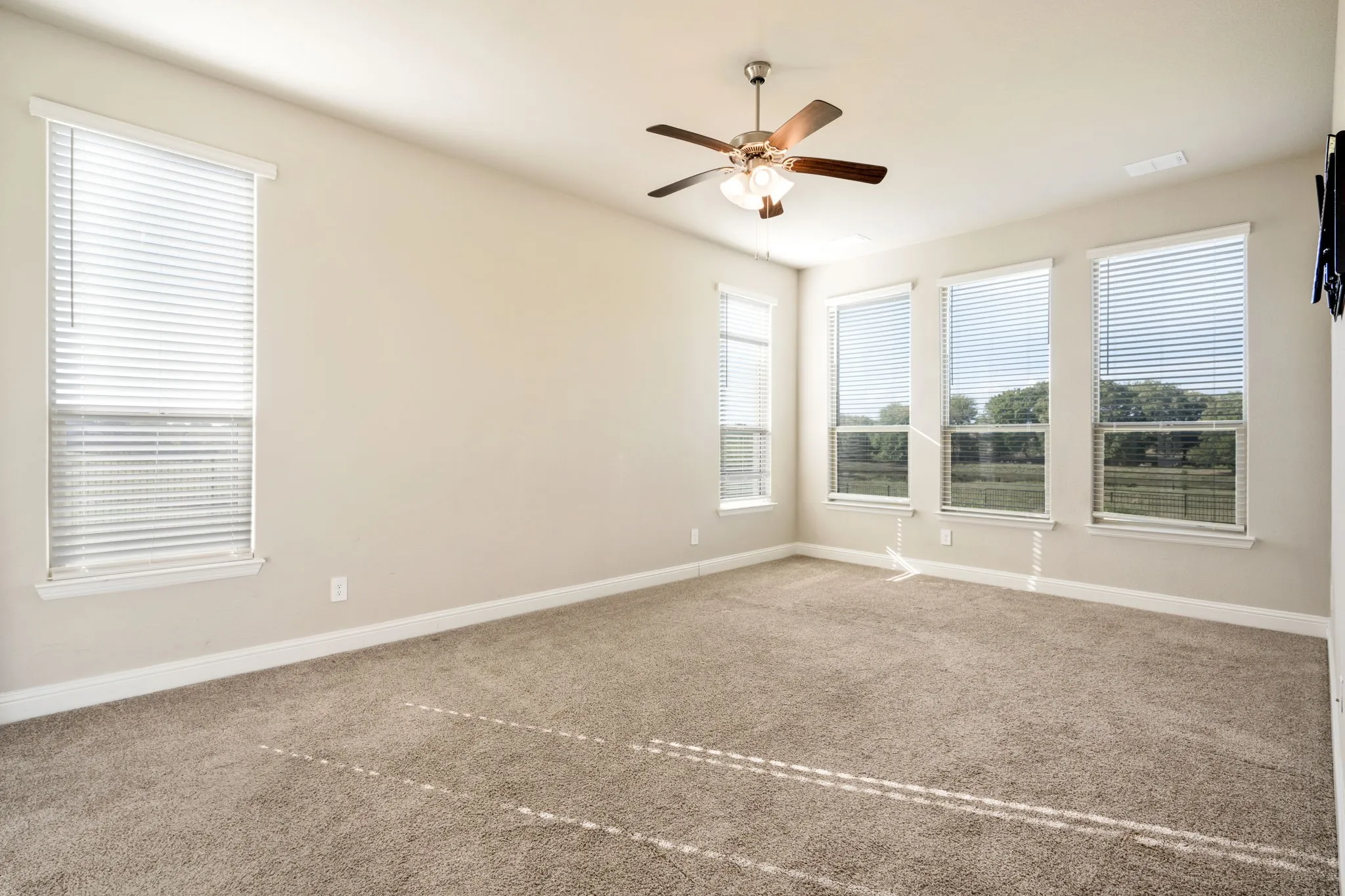 Expansive room featuring multiple windows, neutral wall tones, plush carpeting, and a ceiling fan with integrated lighting