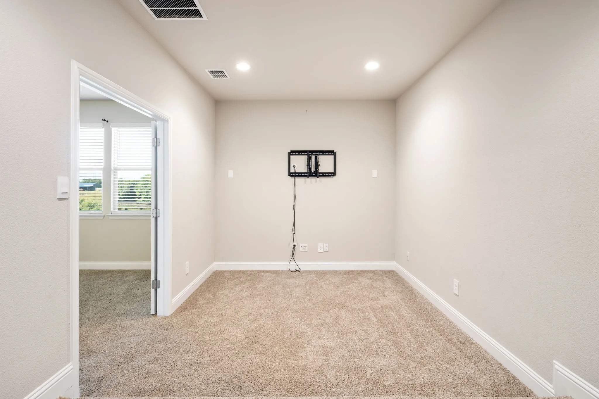 Recessed lighting, wall-mounted television bracket, neutral carpet flooring, white trim, and a glass-paneled door