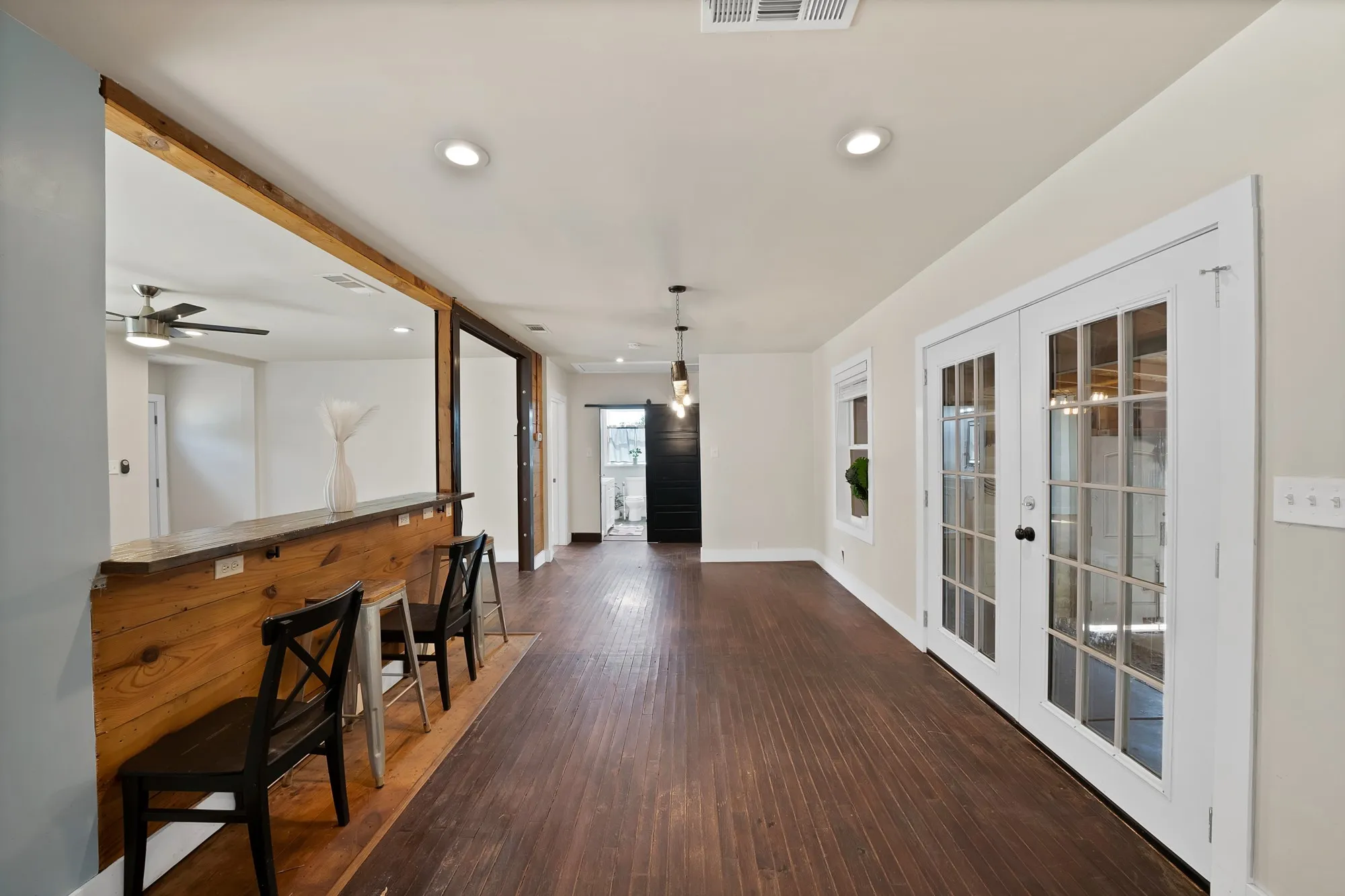 Dining area: Industrial steel I-beam chandelier with Edison bulb pendants, French doors to the covered back patio, and hardwood floors. Open floor plan flows into the kitchen and knotty pine breakfast bar with seating.