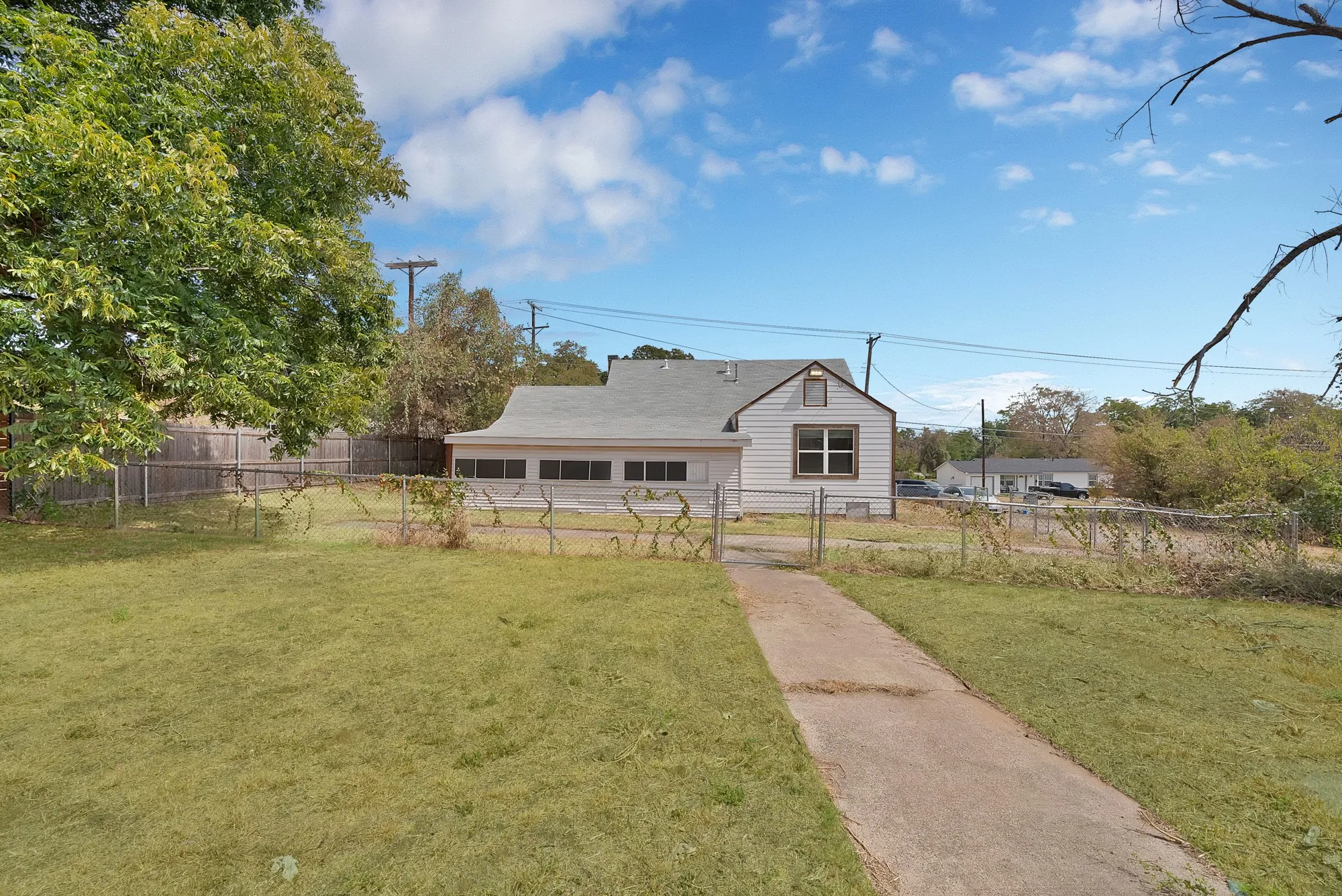 Backyard: Mature shade tree, concrete walkway, and chain link fencing with gate. Rear exterior with gable roof and composition shingle roof.