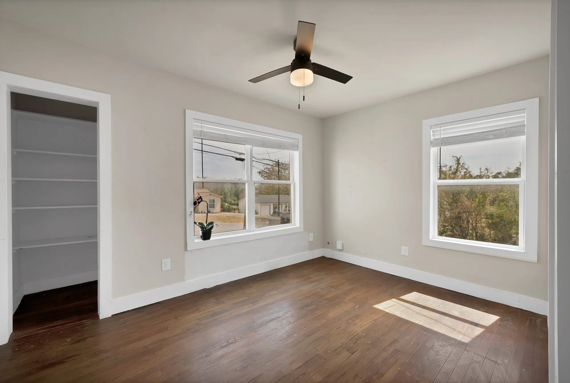 Bedroom: Corner bedroom with two windows, blinds, ceiling fan with light, and hardwood floors. Closet with built-in shelving.