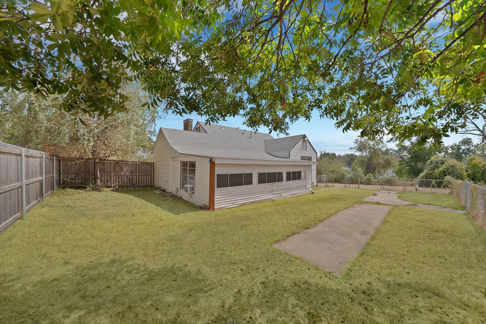 Backyard: Wood privacy fence, mature shade trees, and concrete walkway. Rear exterior shows the enclosed covered patio with a row of windows.