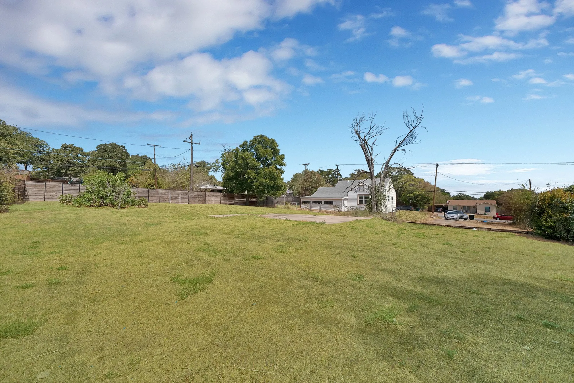 Backyard: Large open grass yard with concrete slab, mature trees, and wood privacy fencing. Room for outdoor living, gardening, or future improvements.