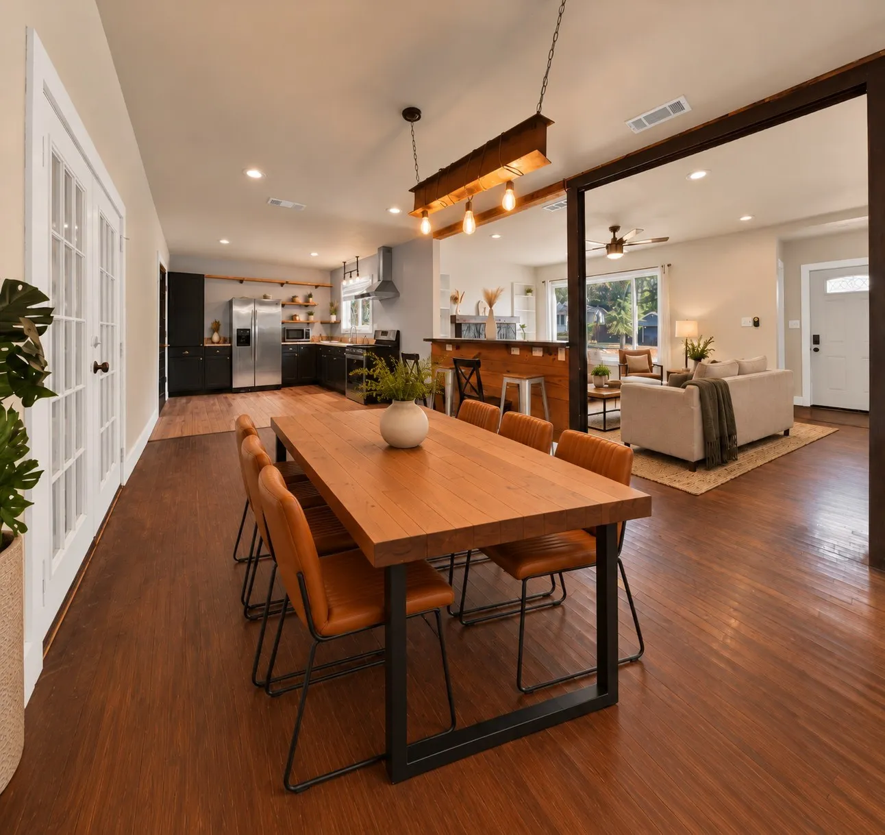 virtually staged Open floor plan: Dining area flows into the kitchen and living room under recessed lighting and a wood beam Edison bulb chandelier. Kitchen features black shaker cabinetry, open wood floating shelves, stainless steel appliances with side-by-side refrigerator, and stainless vent hood.