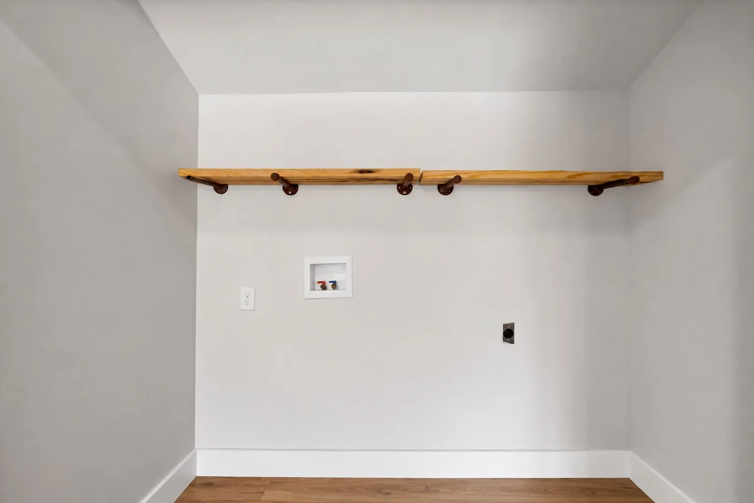 Laundry room: Full-size washer and dryer connections with recessed washer box and electric dryer outlet. Natural wood floating shelf on industrial pipe brackets and wood-look plank flooring.
