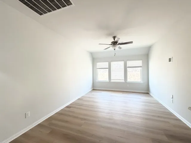 Wood-finish flooring, multiple windows with blinds, ceiling fan, and white walls