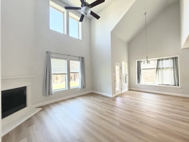 Vaulted ceilings with a ceiling fan, light wood-finish flooring, white mantel fireplace, multiple windows, and a glass-paneled door