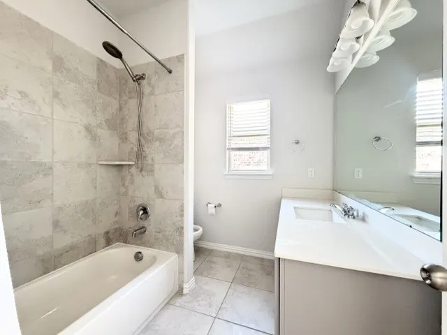 Bathtub with tile surround, shower fixture with handheld spray, single vanity with integrated sink, expansive mirror, and window with blinds
