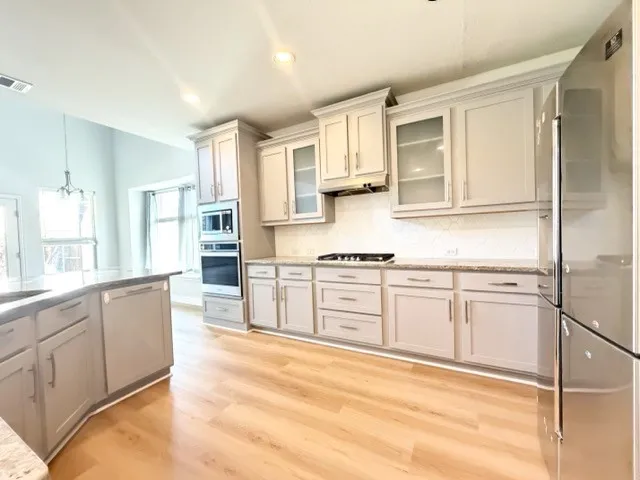 Kitchen featuring light wood-finish flooring, light gray cabinetry, stainless steel appliances, and a white tile backsplash