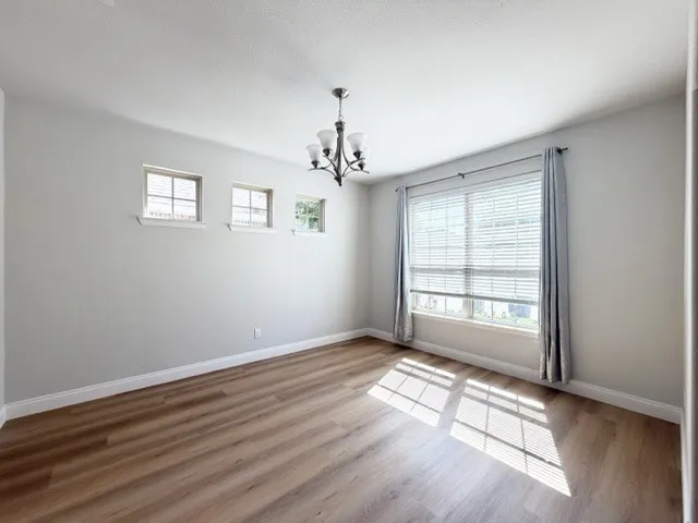 Wood-finish flooring, recessed lighting, and a modern chandelier illuminate this bright room with multiple windows