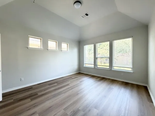 Vaulted ceiling, wood-finish flooring, multiple large windows, additional high windows, and a flush mount ceiling light