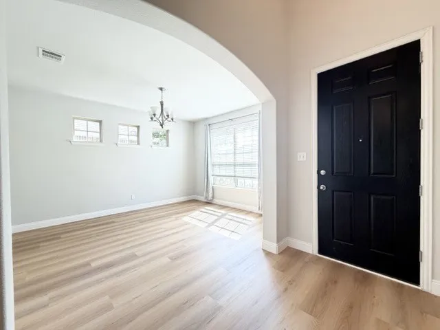 Wood-finish flooring throughout, arched entryway, a black paneled door, and a multi-light chandelier