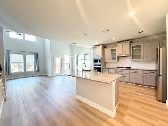 Open-concept living space featuring wood-finish flooring, a kitchen island with stone countertop, stainless steel appliances, and a vaulted ceiling with transom windows