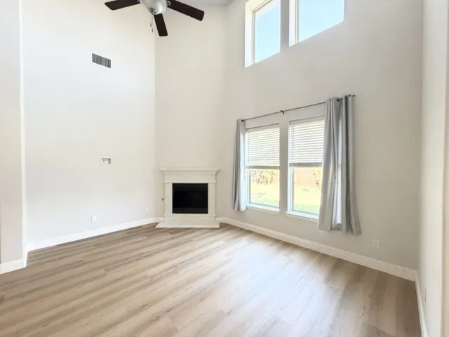 Wood-finish flooring, corner fireplace with classic mantel, high ceilings, multiple windows, and a ceiling fan