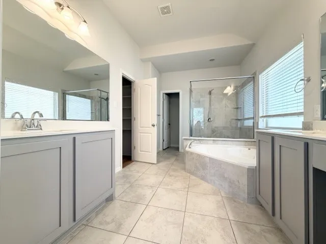 Dual vanity with light gray cabinetry and white countertops, featuring a tiled soaking tub and a separate glass-enclosed shower