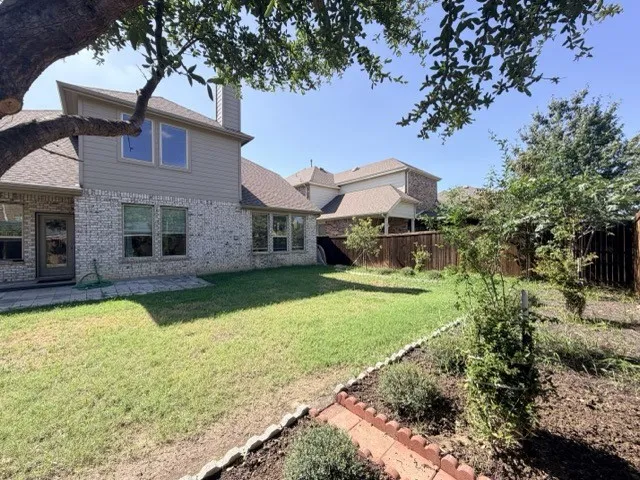 Expansive backyard featuring a manicured lawn, brick and siding exterior, multiple windows, and a paved patio