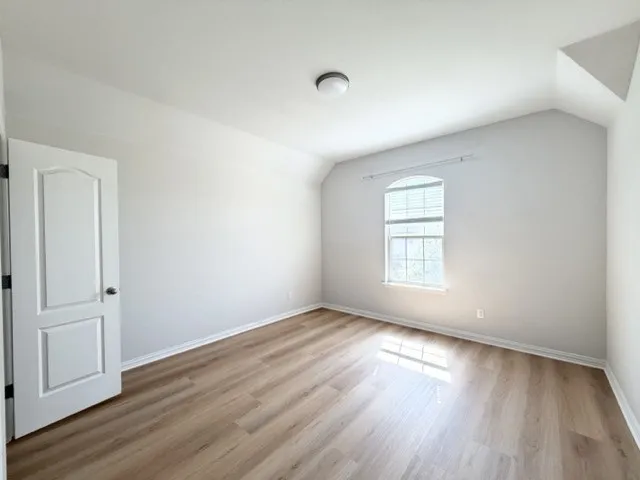 Wood-finish flooring, arched window, recessed window blinds, neutral wall paint, and overhead flush-mount lighting