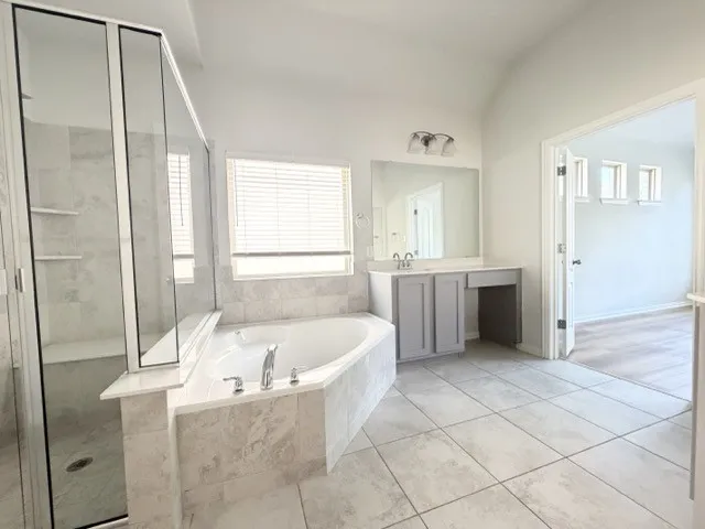 Corner soaking tub, separate glass-enclosed shower, dual vanity, tile flooring, and vaulted ceiling