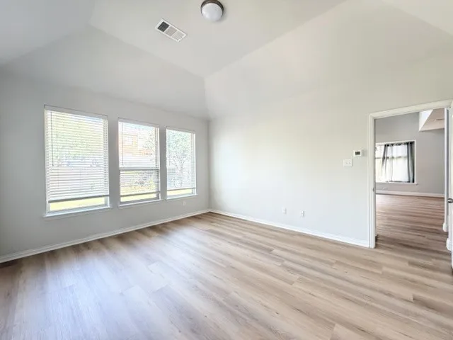 Vaulted ceiling, wood-finish flooring, three large windows with blinds, recessed lighting, and a neutral color palette