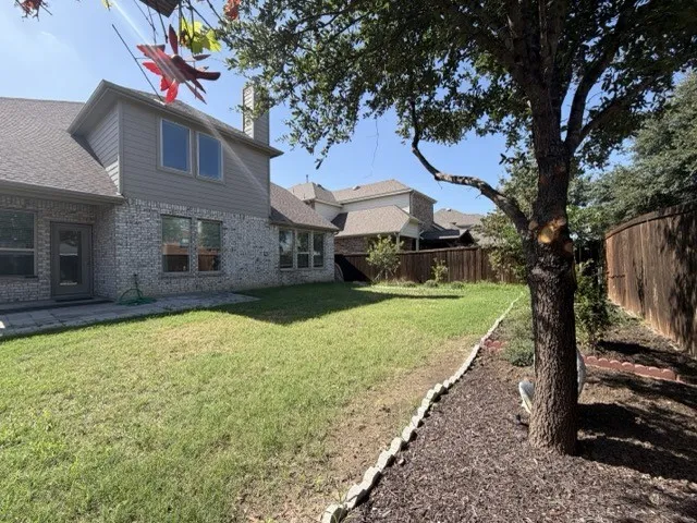Spacious backyard featuring a privacy fence, mature tree, and a brick and siding exterior