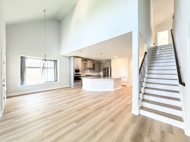 Vaulted ceilings, wood-finish flooring, staircase with dark wood handrail, kitchen island with built-in appliances, stainless steel appliances