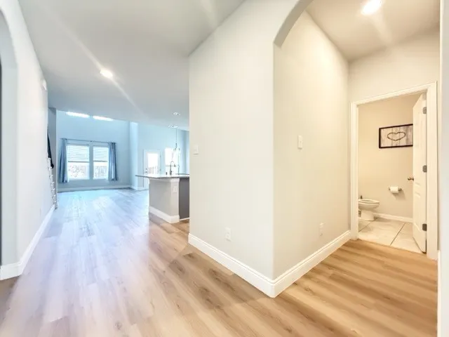 Arched hallway entry leading to an open-concept living area with wood-finish flooring, recessed lighting, and a powder room featuring tile flooring