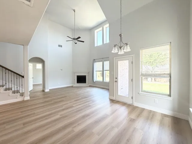 Soaring ceilings with a chandelier, wood-finish flooring, a white mantel fireplace, and a staircase with wrought iron balusters