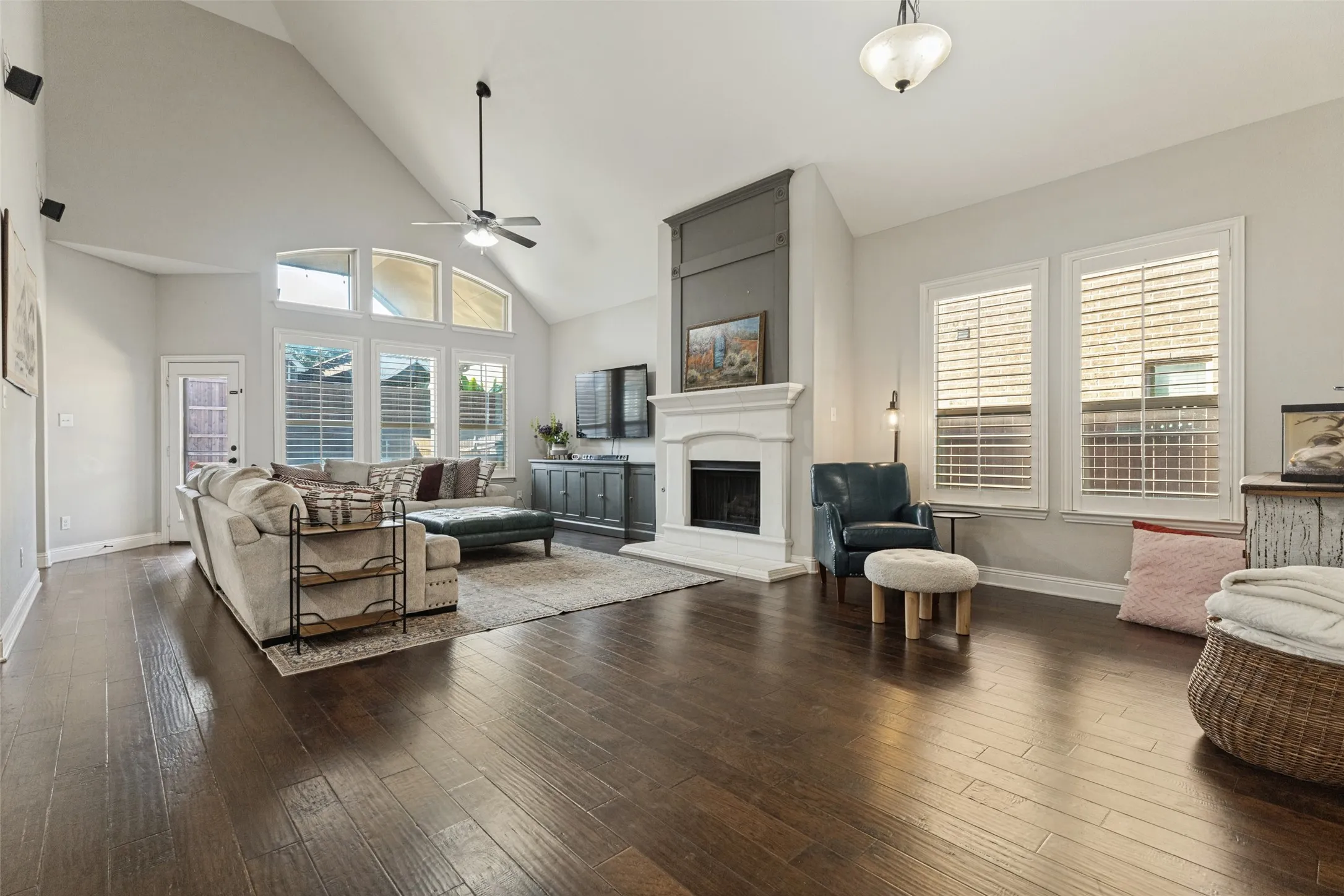 Living room with fireplace, large windows, ceiling fan and dark floors