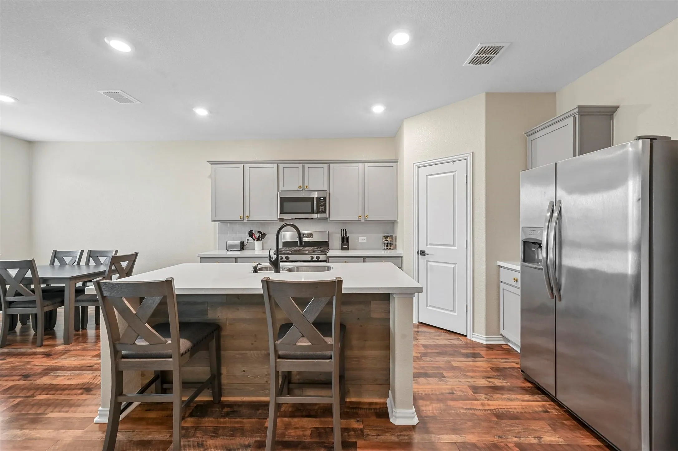 Kitchen with gray cabinetry, dark wood-type flooring, sink, an island with sink, and stainless steel appliances