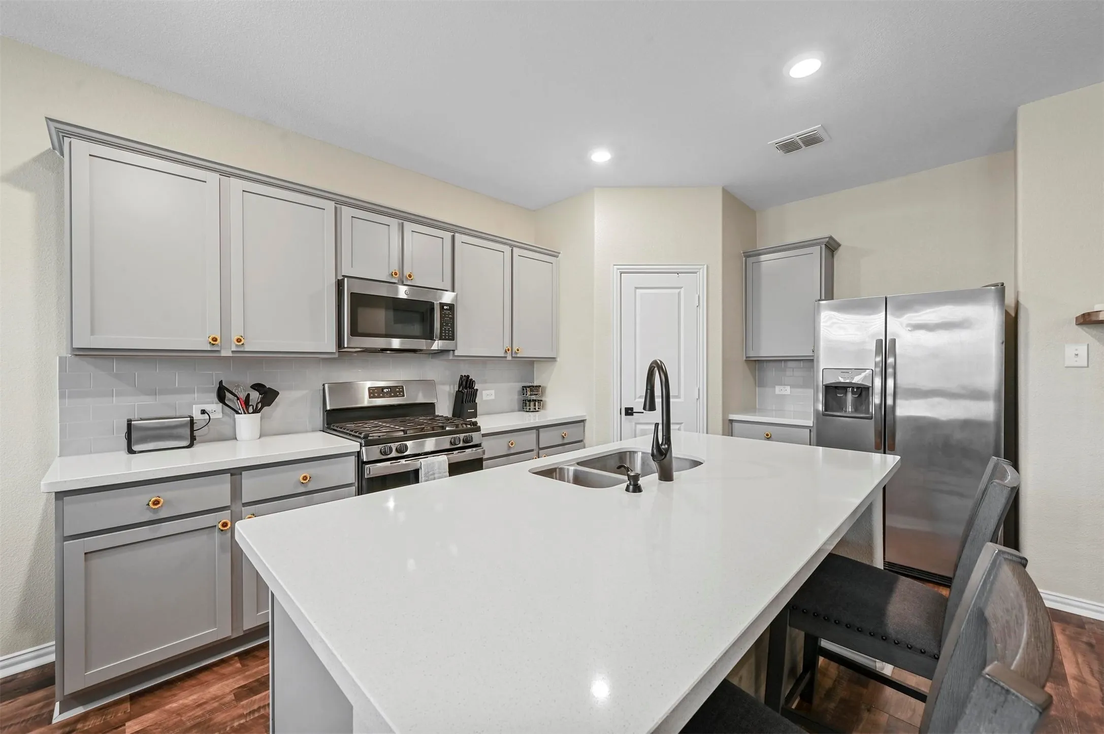 Kitchen with a center island with sink, gray cabinets, sink, and appliances with stainless steel finishes