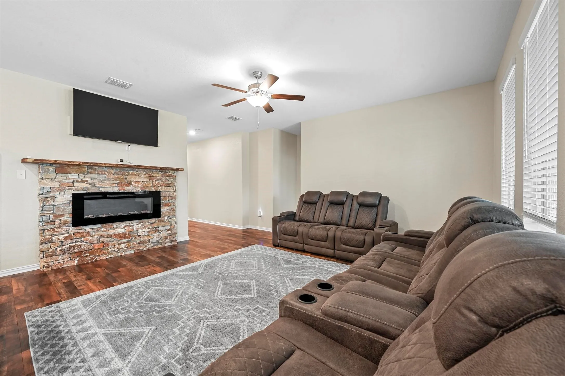 Living room with a stone fireplace, ceiling fan, and dark hardwood / wood-style flooring