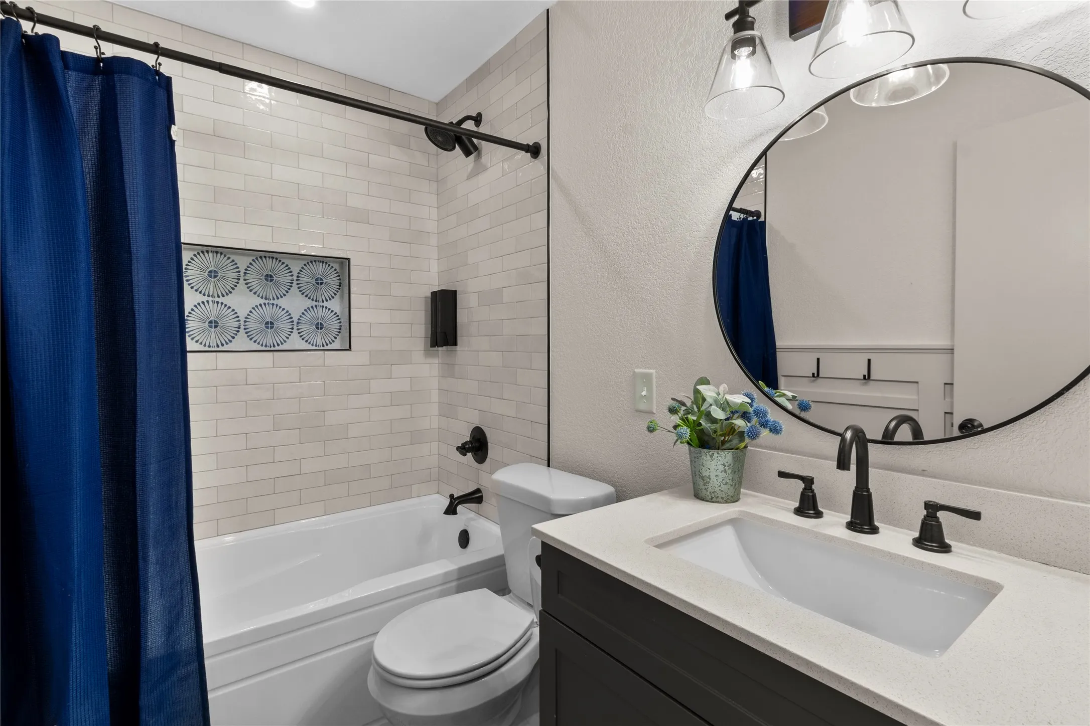 Bathroom featuring white subway tile, a built-in shower niche, a dark wood-finish vanity, a light stone-look countertop, and matte black fixtures