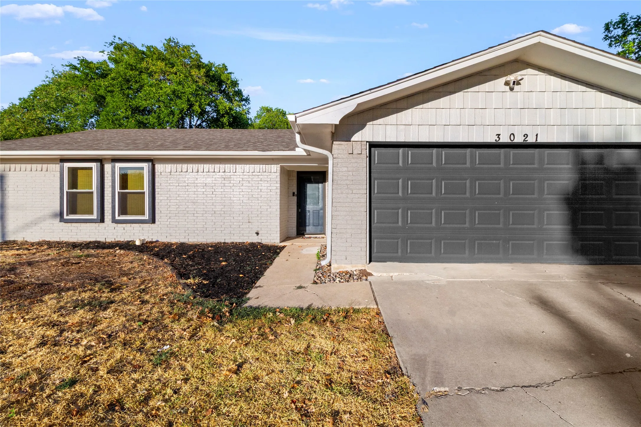 Brick exterior with white paint, dark gray garage door, and a concrete driveway