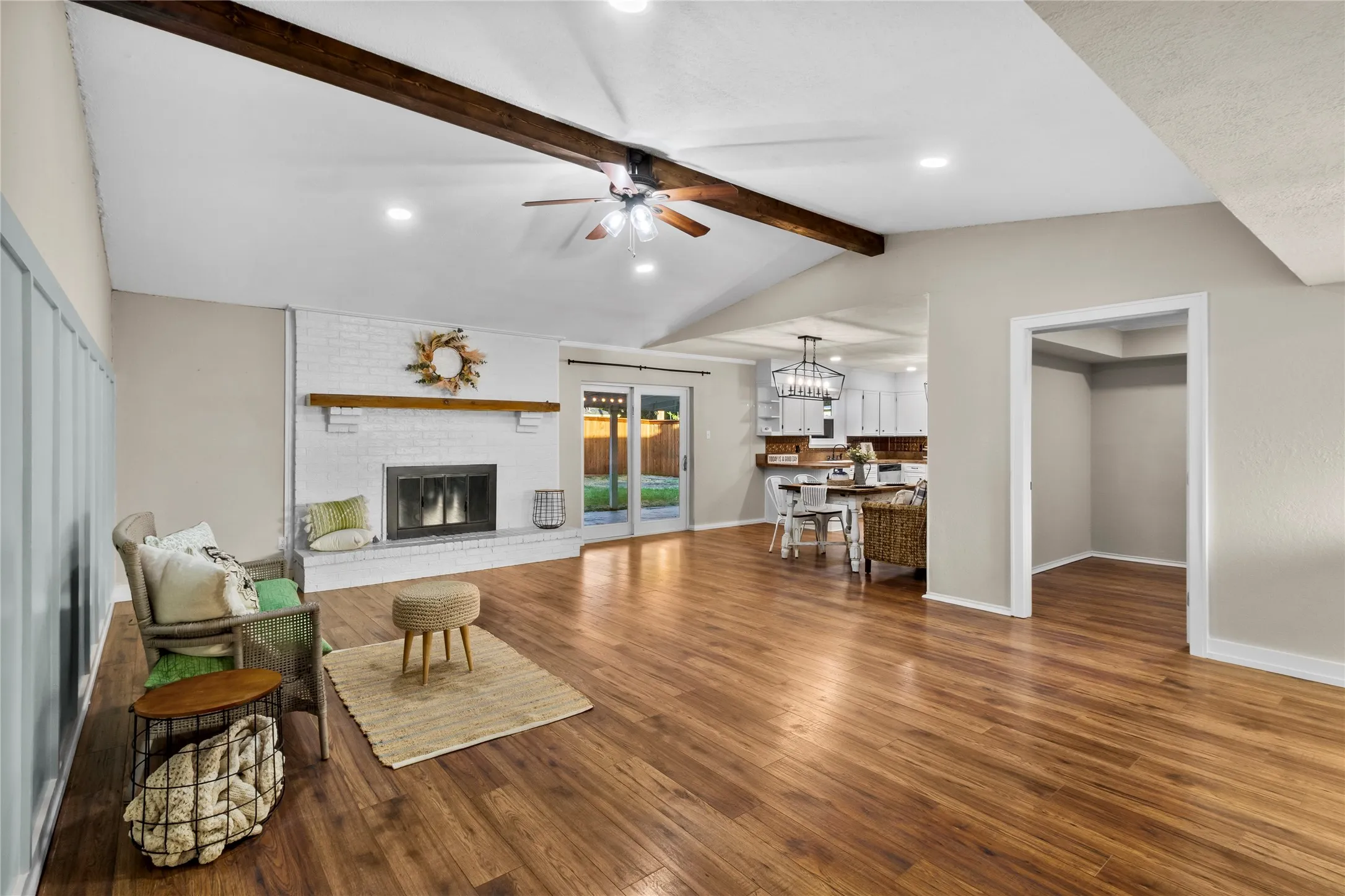 Wood-finish flooring throughout, vaulted ceilings with exposed beams, brick fireplace with wood mantel, sliding glass doors to the backyard, and recessed lighting