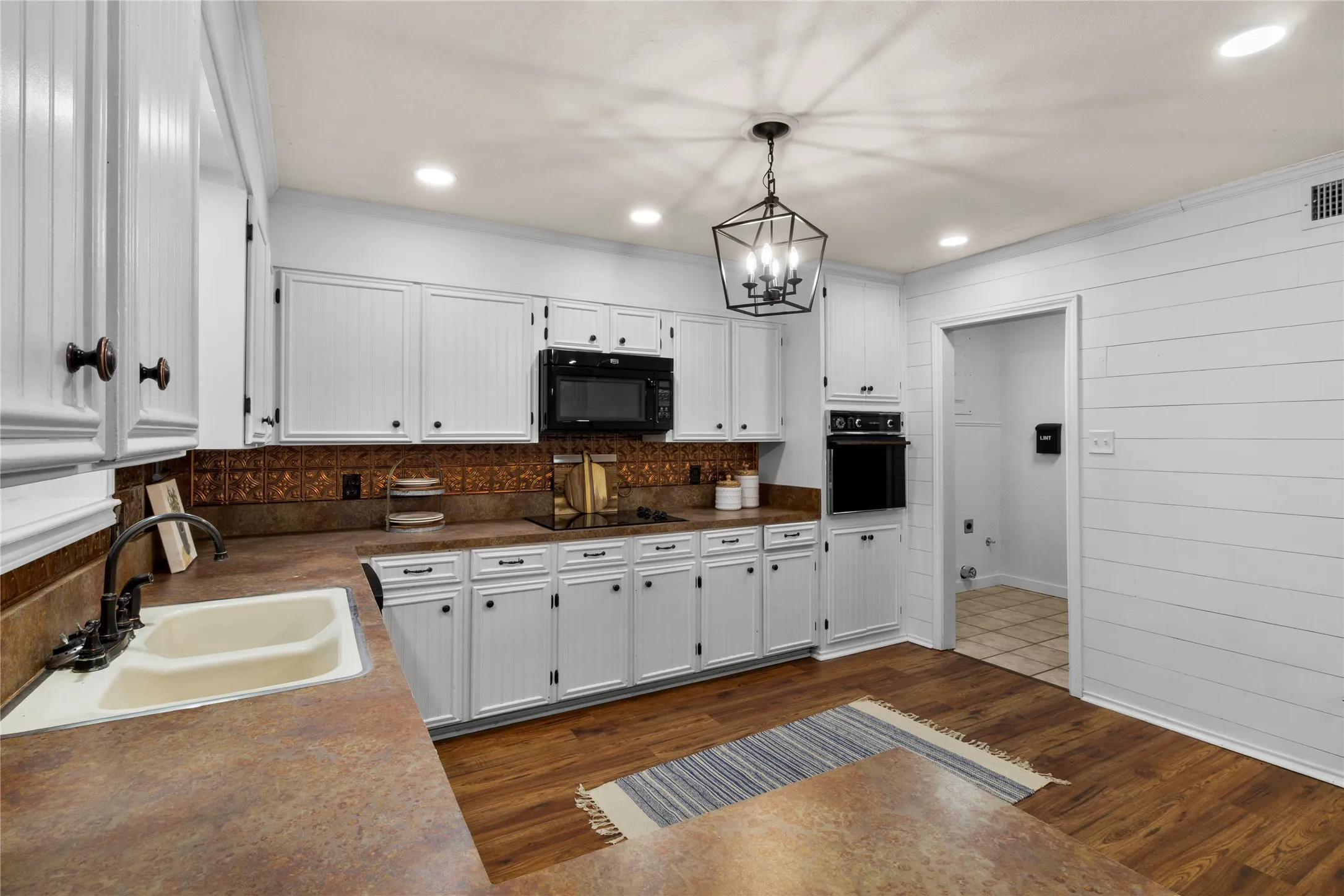 White cabinetry with dark hardware, brown countertops, and a copper-toned backsplash