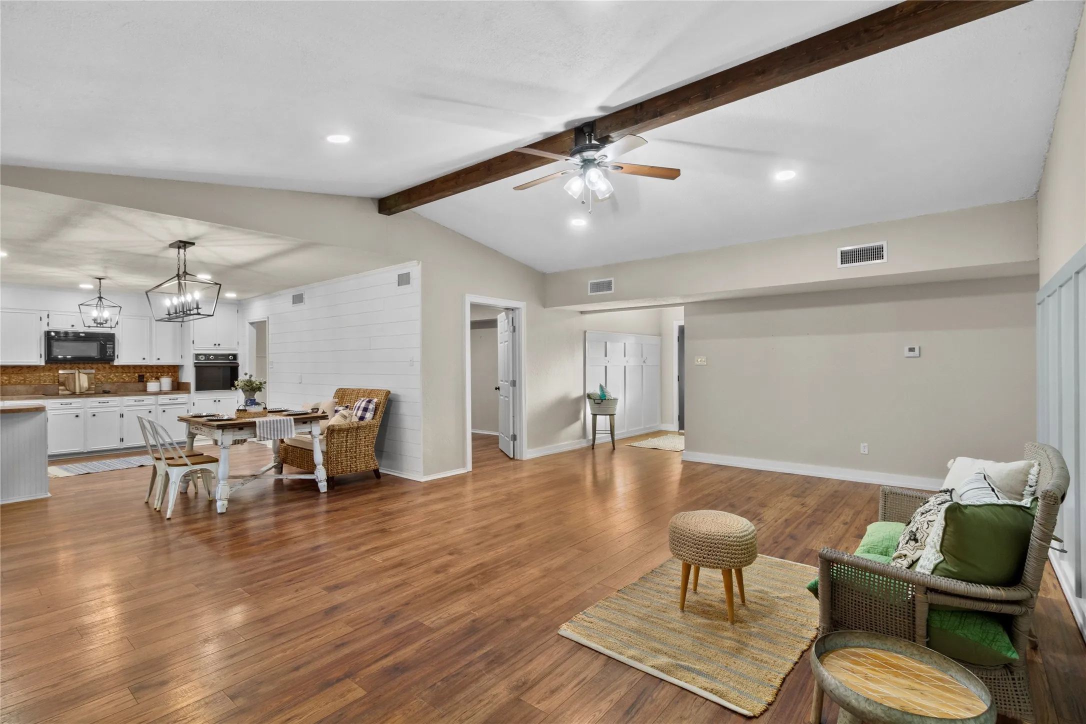Vaulted ceiling with exposed wood beam, wood-finish flooring, white cabinetry, built-in oven, and recessed lighting