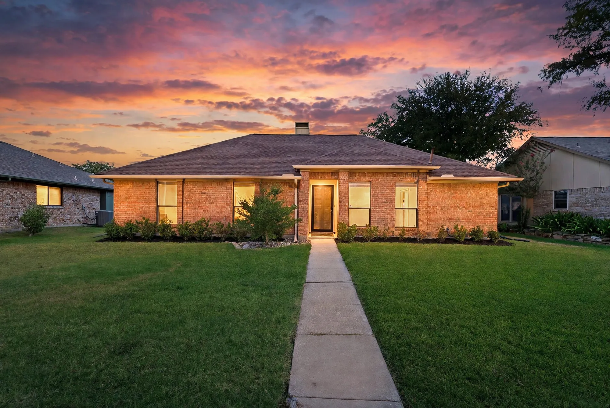 Brick exterior with a dark shingle roof, concrete walkway, and landscaped front yard