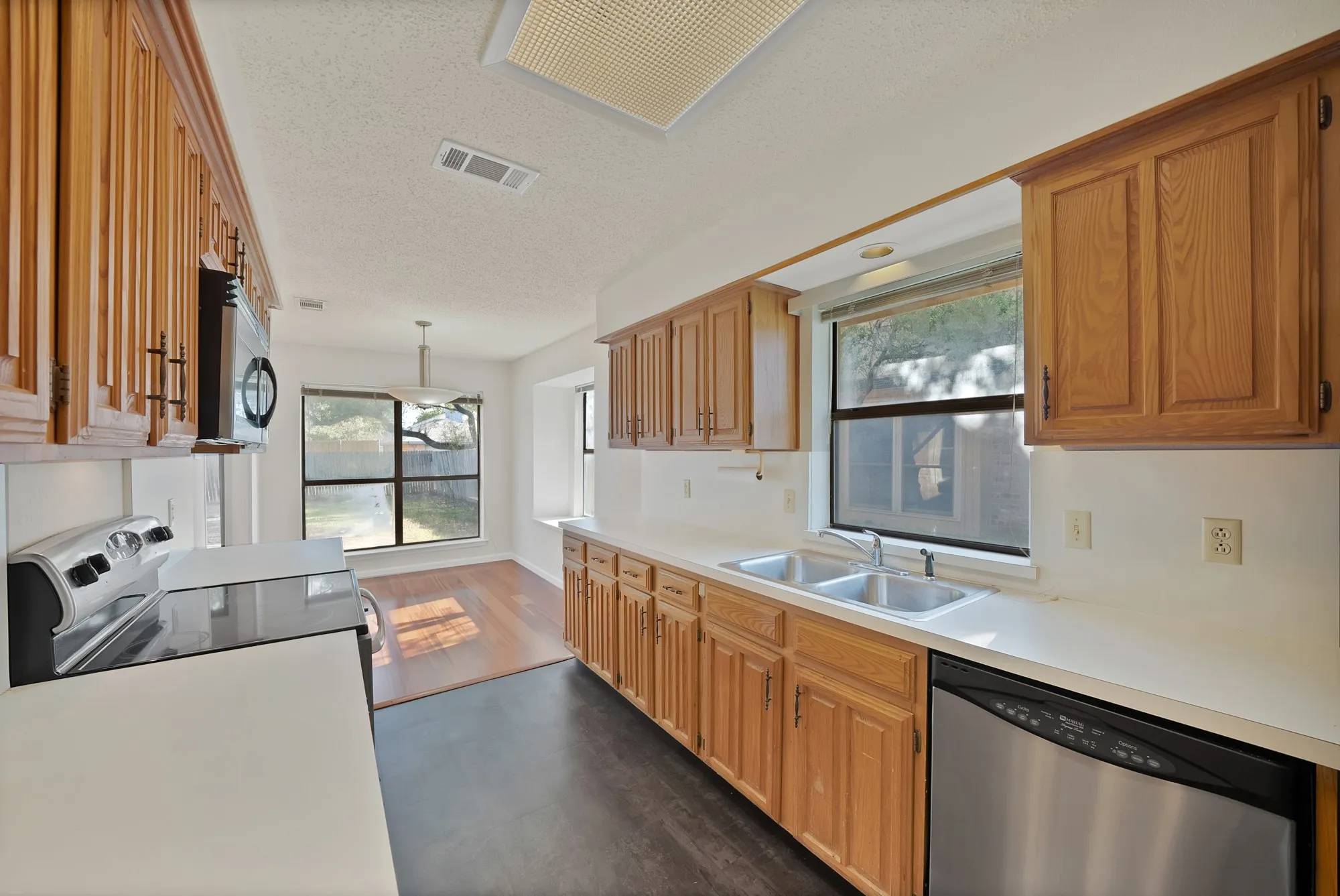 Kitchen featuring wood-finish cabinetry, stainless steel dishwasher, double basin sink, and white countertops