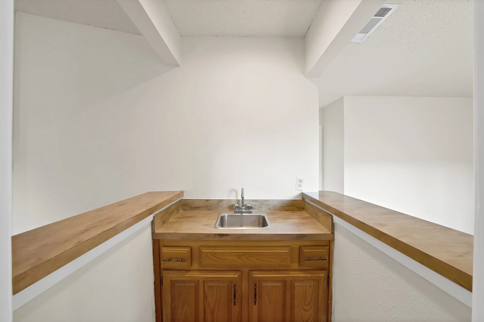 Built-in bar area featuring a stainless steel sink, wood-finish cabinetry, and a countertop with an integrated backsplash