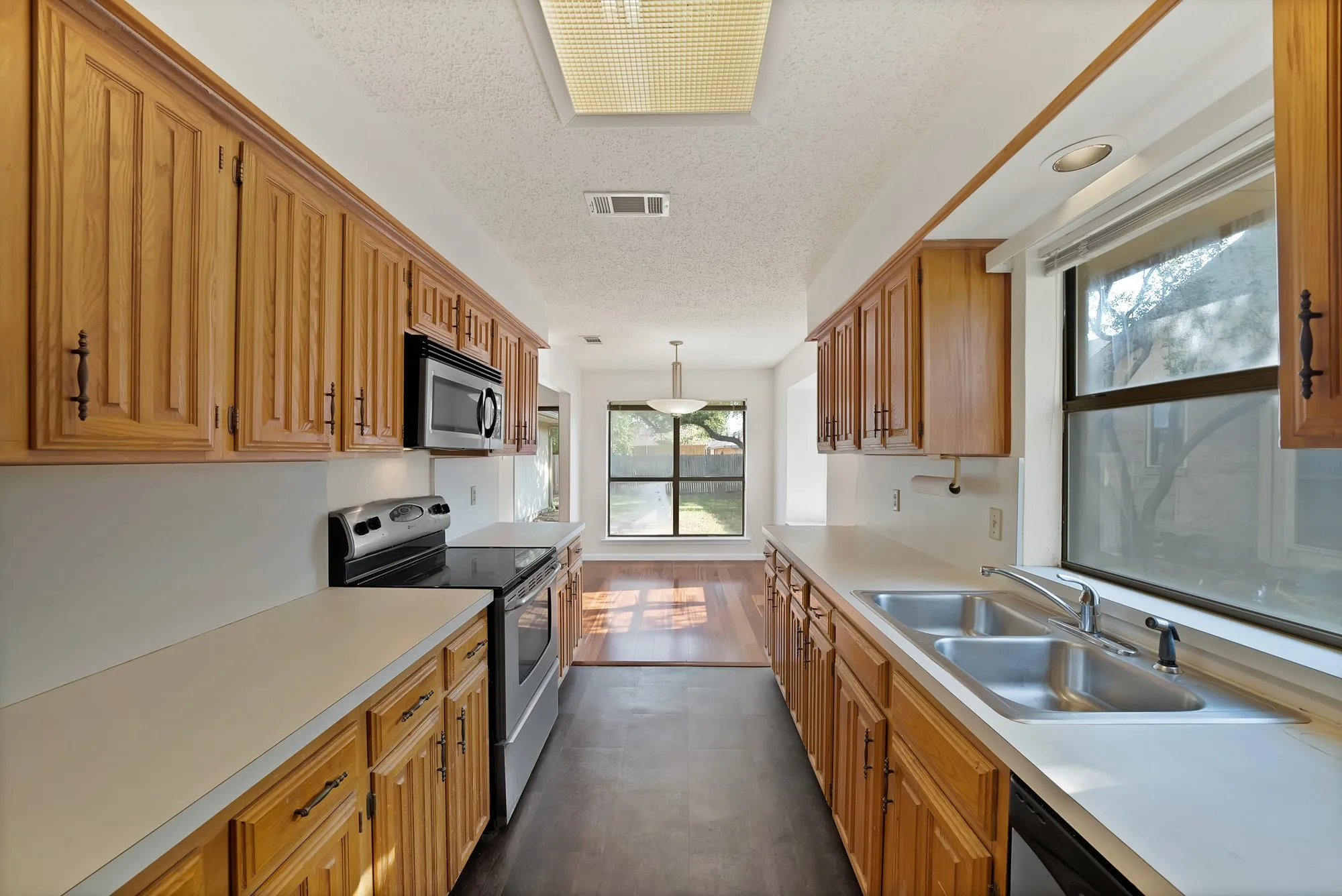 Galley kitchen with wood cabinetry, stainless steel appliances, dual basin sink, and ample countertop space