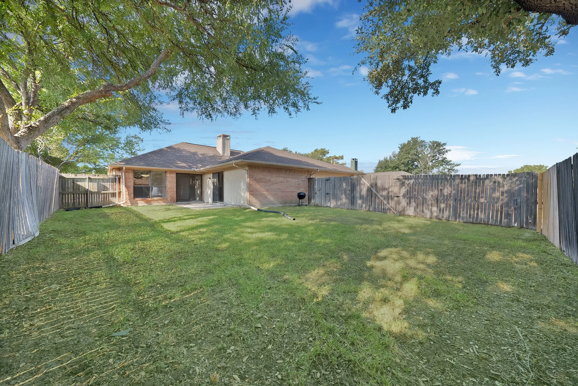 Expansive backyard featuring a manicured lawn, full privacy fencing, and mature trees