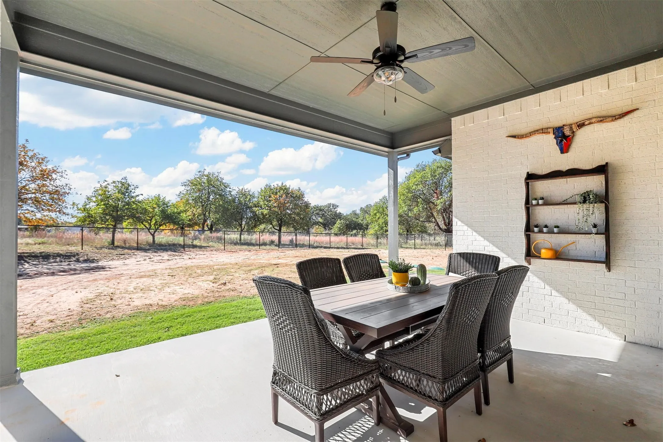 Covered patio with a concrete surface, white brick wall, and a ceiling fan