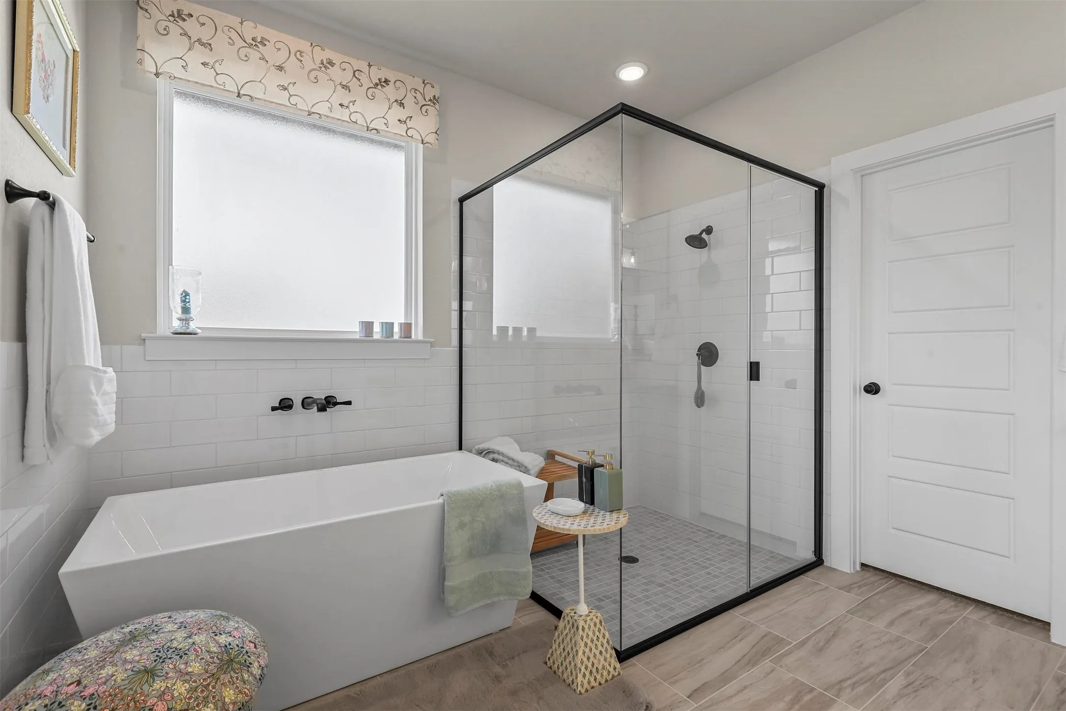 Freestanding soaking tub with wall-mounted fixtures, enclosed shower with black frame, white subway tile surround, and wood-finish flooring