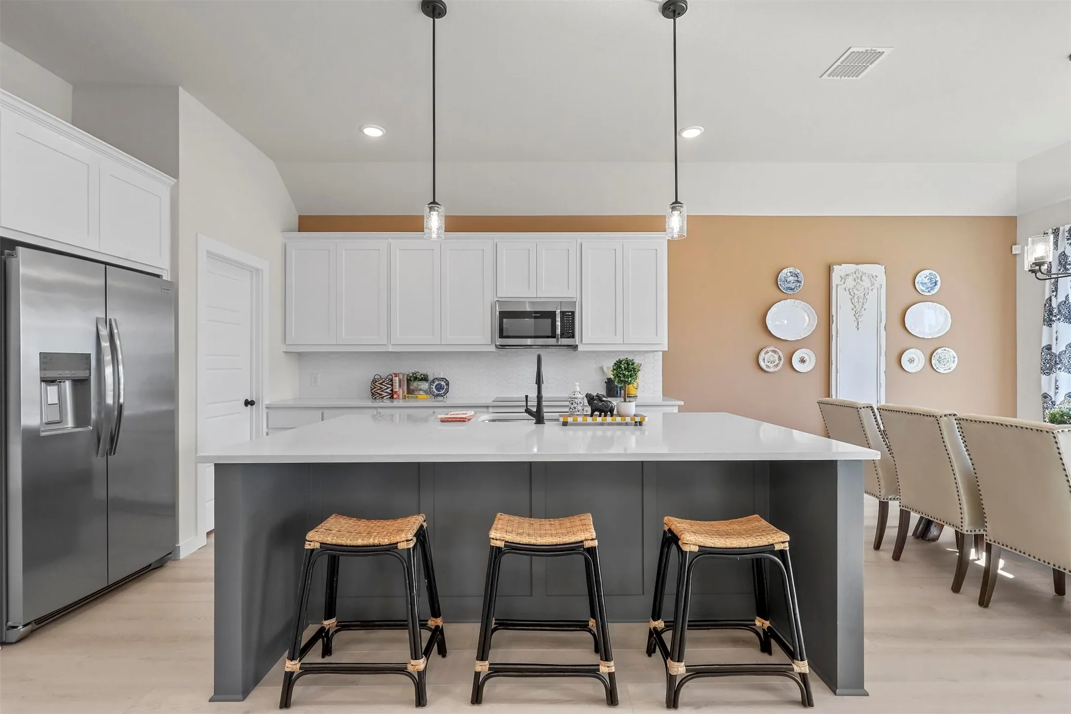 Modern kitchen featuring an island with seating, white cabinetry, integrated stainless steel appliances, pendant lighting, and light wood-finish flooring
